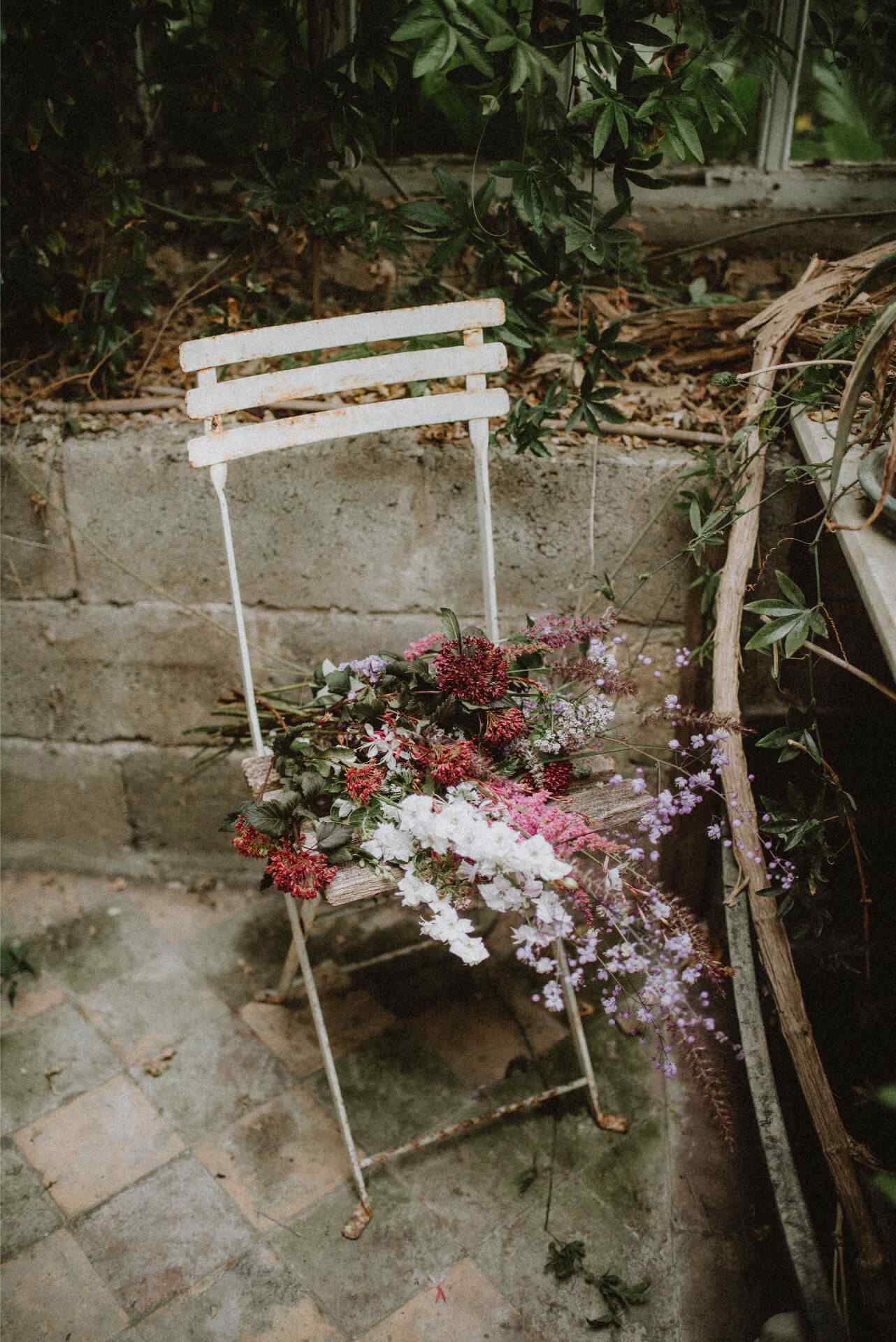 A rustic metal garden chair with purple and white cut flowers lying on it