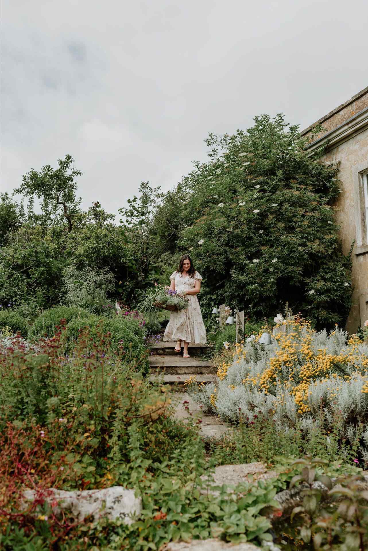 A woman climbs down garden steps holding a trug of freshly cut cottage garden flowers