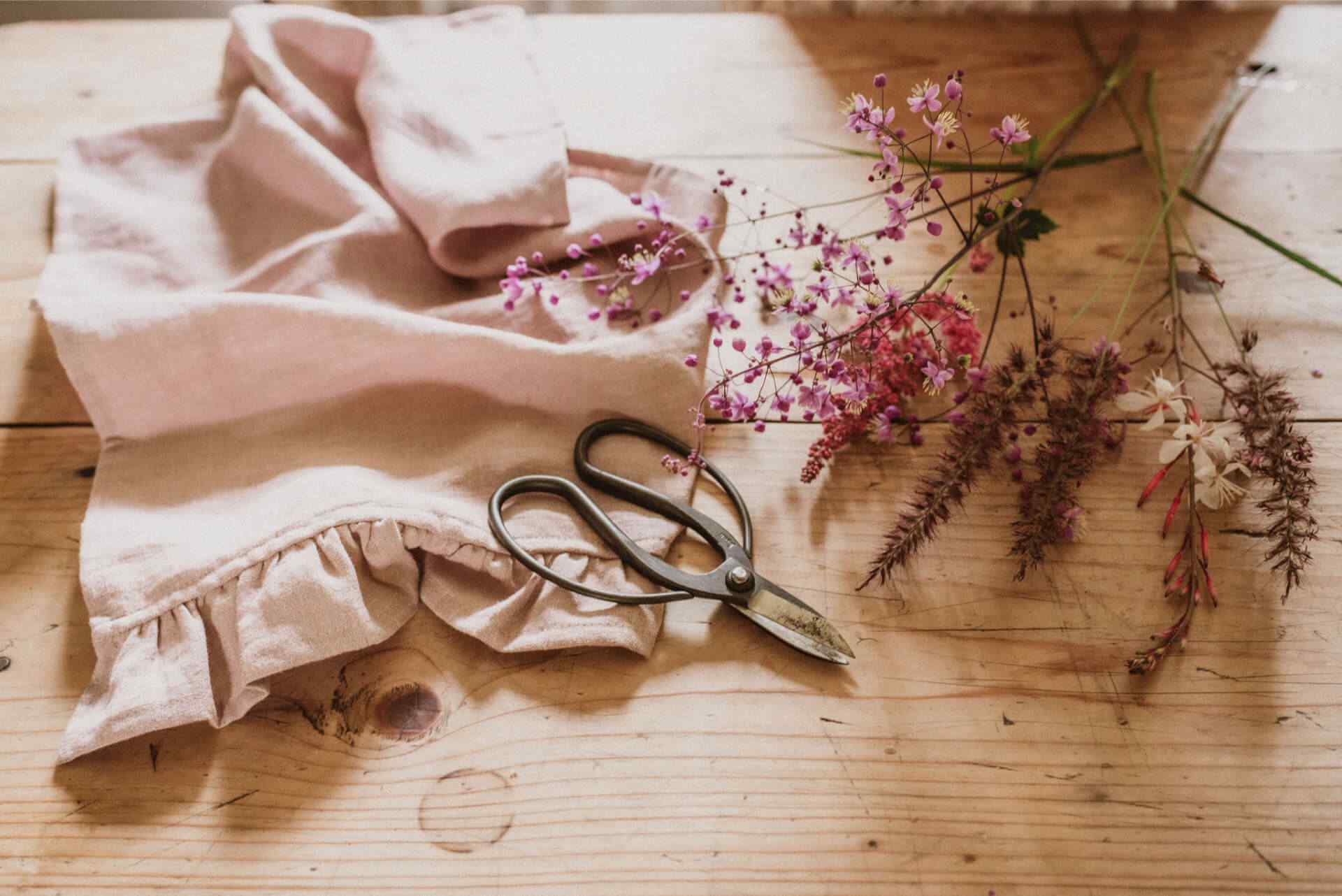 Flowers, floristry snips and a pink tea towel lie on a rustic kitchen table